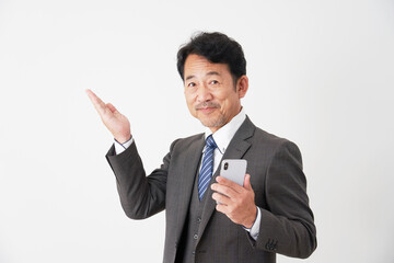 スマホを持って手の平で左側を指す中年のビジネスマン　白背景