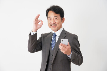 スマホを持ってOKポーズをする中年のビジネスマン　白背景