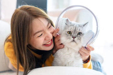 Spending your free time at home with your cat. young asian woman get in headphones for cat, lies on floor in living room, with fluffy Maine Coon cat, listens to music