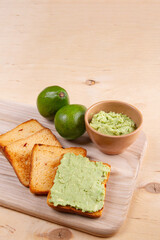 Guacamole adorn toasted tomato bread on wooden cutting board, highlighting the presence of avocado fruits. Vertical banner