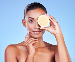 Portrait, woman and lemon on eyes in studio for vitamin c cosmetics, eco friendly beauty or detox. Face of indian model, healthy skincare or citrus fruit of sustainable dermatology on blue background