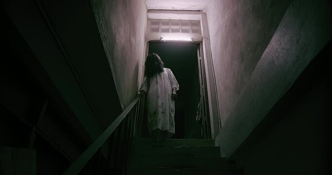 Horror scene of a mysterious Scary Asian ghost woman creepy have hair covering the face standing on staircase at abandoned house with background dark scene movie at night, festival Halloween concept