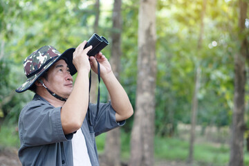 Fototapeta premium Asian man ecologist use binocular to survey nature in forest. Concept, nature exploration. Ecology study. Pastime activity, lifestyle. Explore environment. Traveling alone 