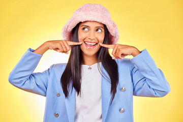 Fashion, smile and face of Indian woman on yellow background with silly, goofy and playful expression. Emoji, happiness and person in studio pointing to mouth in trendy accessories, style and hat - obrazy, fototapety, plakaty