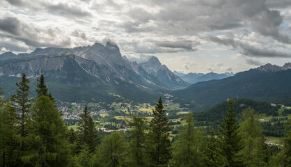 View on the surrounding mountains of Cortina D'Ampezzo in Italy from Tofana mountain. Pine trees in the foreground, mountain range in the background. Cloudy summer day.