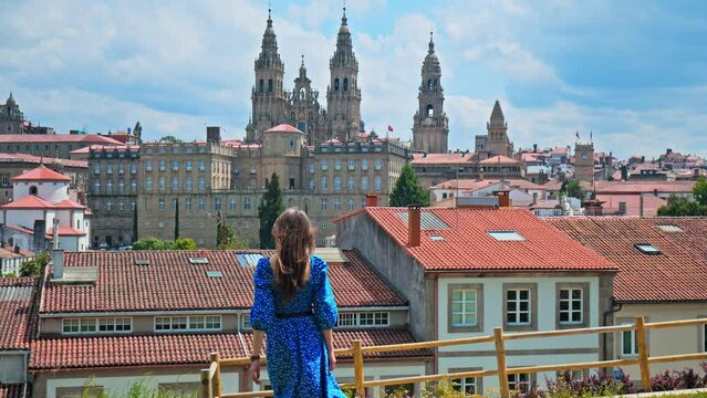 A tourist girl looking at the Cathedral of Santiago de Compostela with a panoramic city view in Spain. A female walking towards the famous Spanish Basilia a World Heritage Site in Galicia, Spain.