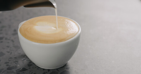 Pour steamed milk to make cappuccino on concrete countertop
