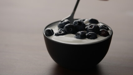 scoop organic yogurt with blueberries in black bowl on wood table
