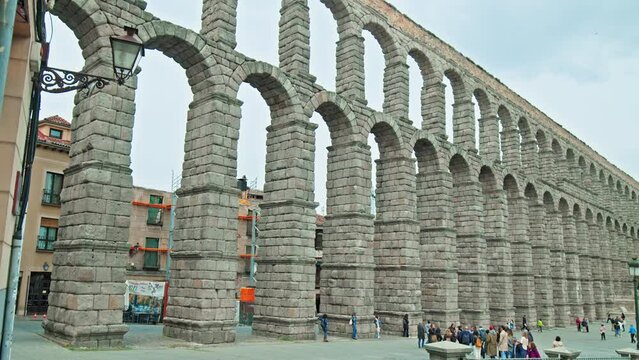 Tourists visiting the famous Aqueduct of Segovia in Castile and Le&oacute;n region. People explore a historic city northwest of Madrid in Spain with a Towering Roman aqueduct and grand landmark monument.