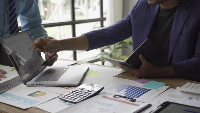 Two young asian businessmen in suits discussing financial market data in office Business team working with charts Stock traders analyze statistics Dynamics shown on graphs
