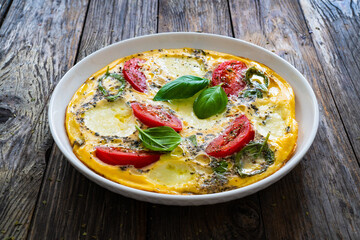 Omelette - scrambled eggs with mozzarella cheese and tomatoes on wooden table
