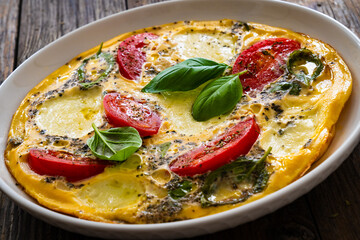 Omelette - scrambled eggs with mozzarella cheese and tomatoes on wooden table
