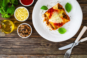 Crepes stuffed with seared minced meat and mozzarella in tomato sauce on wooden table
