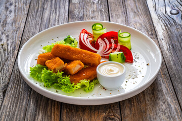Fried fish sticks with fresh vegetables on wooden table
