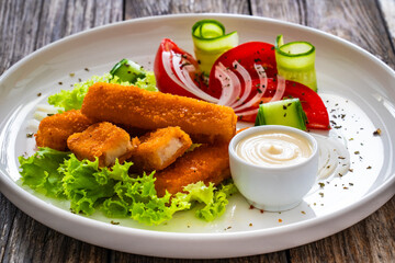 Fried fish sticks with fresh vegetables on wooden table
