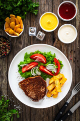 Grilled beef steak with French fries and fresh vegetables on wooden table
