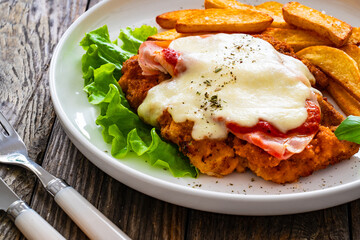 Milanesa Napolitana - fried breaded cutlet with ham, mozzarella cheese and tomato sauce on wooden...