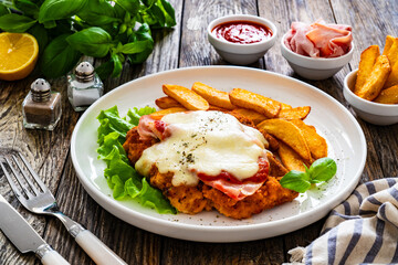 Milanesa Napolitana - fried breaded cutlet with ham, mozzarella cheese and tomato sauce on wooden background - obrazy, fototapety, plakaty