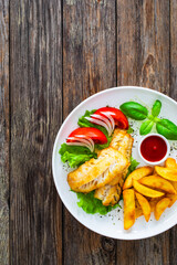 Seared cod loin with fried potatoes and fresh vegetables on wooden table
