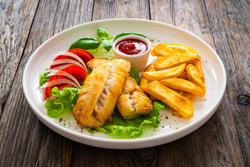Seared cod loin with fried potatoes and fresh vegetables on wooden table