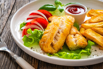Seared cod loin with fried potatoes and fresh vegetables on wooden table
