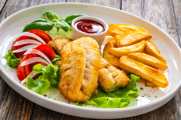 Seared cod loin with fried potatoes and fresh vegetables on wooden table
