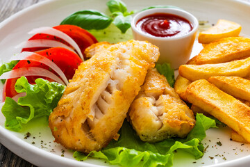 Seared cod loin with fried potatoes and fresh vegetables on wooden table
