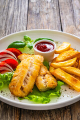 Seared cod loin with fried potatoes and fresh vegetables on wooden table
