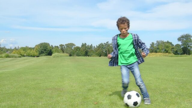 Skillful adorable school age African American boy football player running on field, dribbling , performing tricks and feints, showing individual control of soccer ball while playing game outdoors.