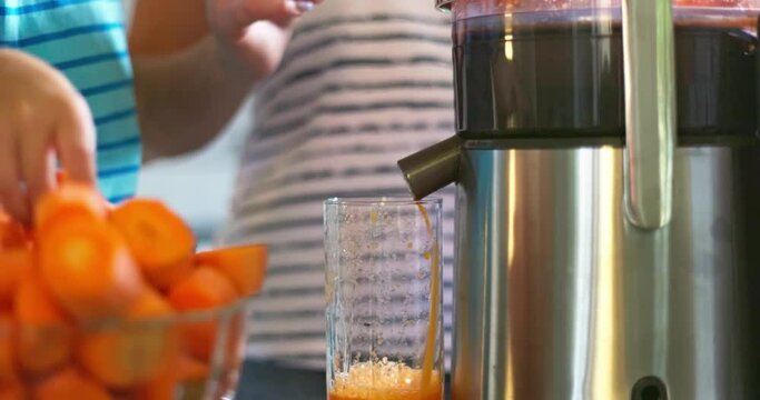 Mother and her son make fresh carrot juice together using juicer in the kitchen