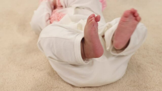 Closeup shot of newborn baby's feet, wearing bodysuit with diaper comfortable lying at home, newborn chubby leg bodypart movement in bed, healthy infant girl try to move tiny feet, childbirth concept.