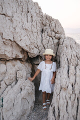 Adorable little girl stand between the rocks and peeking out to camera