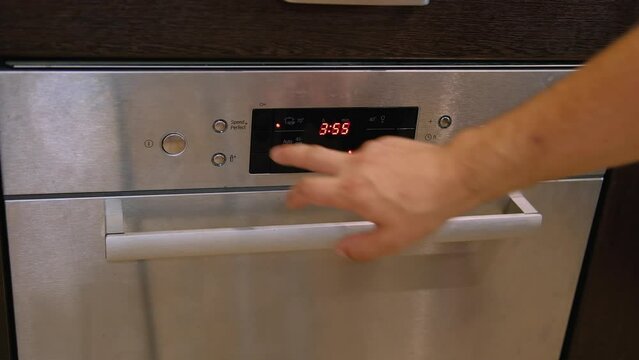 A young man closes the dishwasher and selects the mode and starts it
