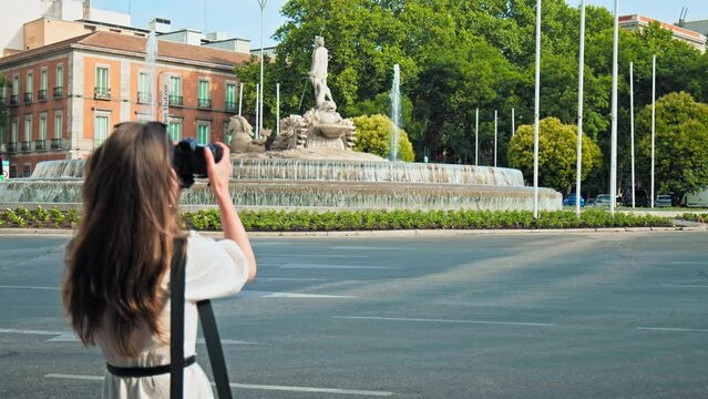 A girl tourist looking at the Cibeles Fountain in Madrid the Capital of Spain. A woman photographing Neoclassical fountain depicting Cybele on a chariot pulled by 2 lions.