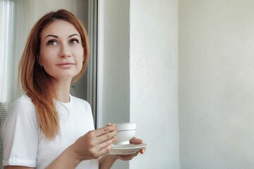 Pensive middle age cute woman drinking coffee on balcony at home and thinking, thought looking away. Adult lovely lady with cup in hands drinks morning tea. Home lifestyle concept. Copy ad text space - Powered by Adobe