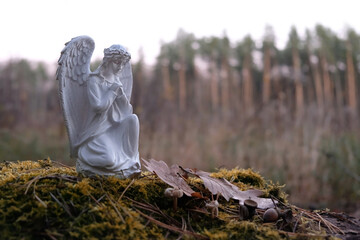 Praying angel figurine close up in autumn forest, natural blurred background. symbol of faith in...