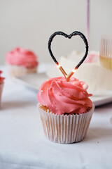 Cupcake with pink whipped cream and burnt-out candle in the form of a heart close-up on a white background. holiday birthday