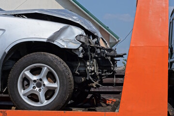 part of a gray broken passenger car after an accident stands on the orange metal of a tow truck on the street - obrazy, fototapety, plakaty