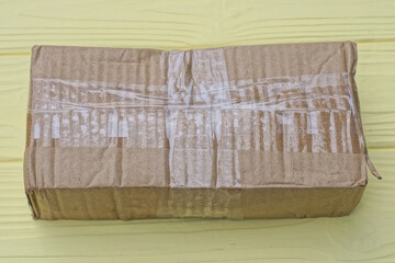 one brown paper closed rectangular parcel cardboard box lies on a yellow wooden table
