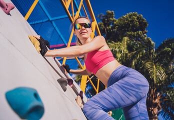 Athletic young woman working out and climbing at the artificial rock in training camp.