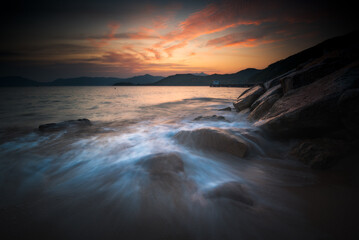 sunset over the sea with water flow and rock in foreground