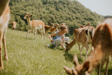 Little girl among reindeer herd on the sunny day