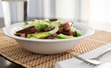 Salad of black tomatoes, avocado and onions in white ceramic bowl