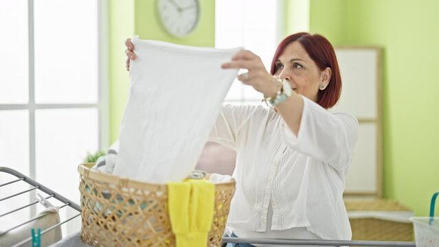 Middle age woman smiling confident holding clothes of basket at laundry room
