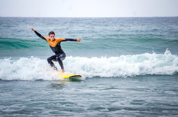 Young Surfer with Neoprene Standing Up on His Board in Balance Position with His Arms to Stand in the Sea Wave