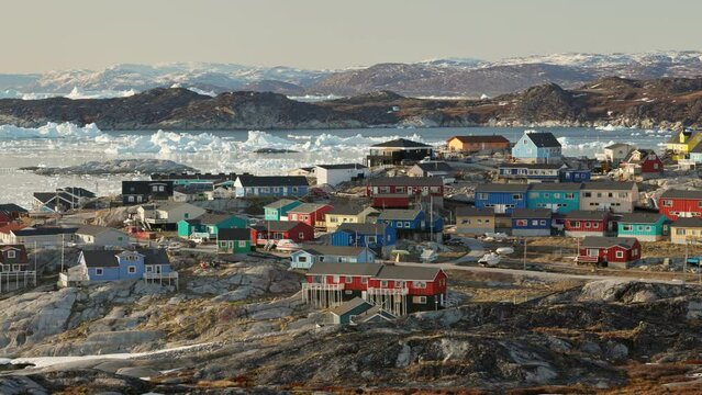 Panning shot of arctic settlement above Arctic Circle against the backdrop of glaciers and icebergs. Village with colorful houses - Ilulissat, Greenland. Nature of Greenland