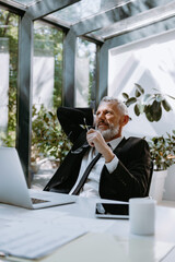 Dreamful mature businessman holding hand behind head while sitting at his working place in office