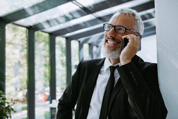 Confident mature businessman talking on mobile phone while standing in the modern office