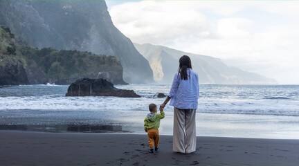 Mother and little child holding hands walking at sea side