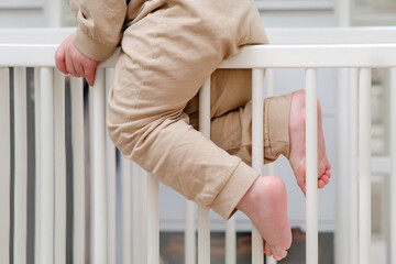 Baby escapes from the crib by climbing over the bars. The child climbs over the bed rail. Kid aged about two years (one year nine months)